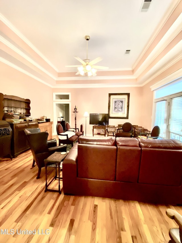 living room featuring a tray ceiling, crown molding, ceiling fan, and light wood-type flooring