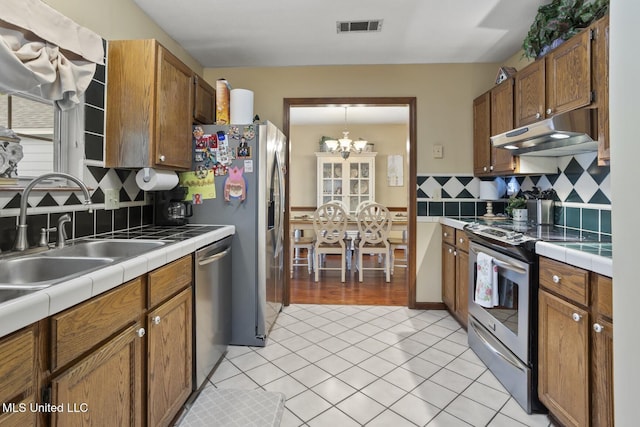 725 Bay Tree Dr, Flowood, MS 39232 - kitchen featuring under cabinet range hood, stainless steel appliances, tile countertops, and a chandelier