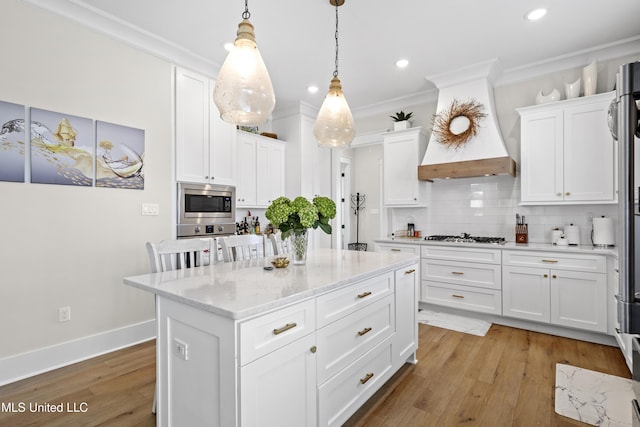 kitchen featuring stainless steel appliances, decorative backsplash, decorative light fixtures, a kitchen island, and white cabinets