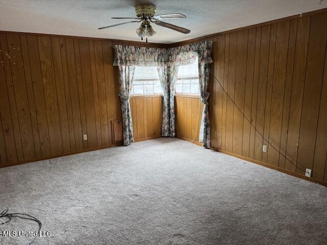 carpeted spare room with ceiling fan, a textured ceiling, and wood walls