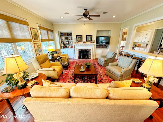 living room featuring wood finished floors, ceiling fan, ornamental molding, built in shelves, and recessed lighting