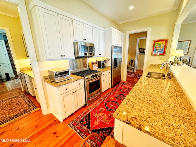 kitchen with appliances with stainless steel finishes, white cabinets, sink, and light hardwood / wood-style floors