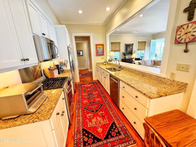 kitchen featuring appliances with stainless steel finishes, a sink, wood finished floors, white cabinets, and light stone counters