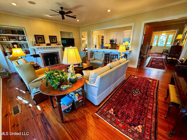 living area featuring crown molding, a ceiling fan, hardwood / wood-style flooring, a fireplace, and recessed lighting
