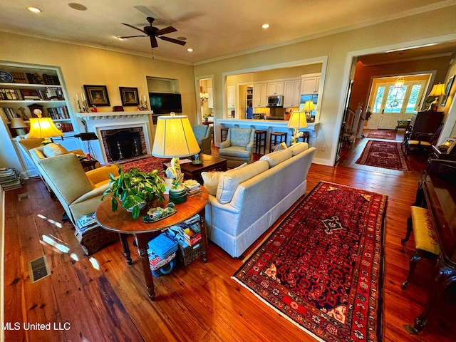 living room with ornamental molding, wood-type flooring, and ceiling fan