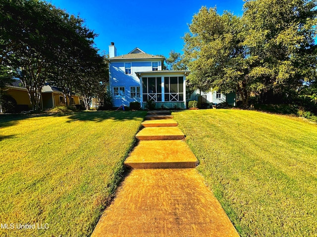 back of property with a sunroom, a chimney, and a lawn
