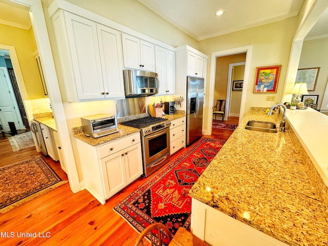 kitchen featuring stainless steel appliances, a sink, light wood finished floors, white cabinetry, and recessed lighting