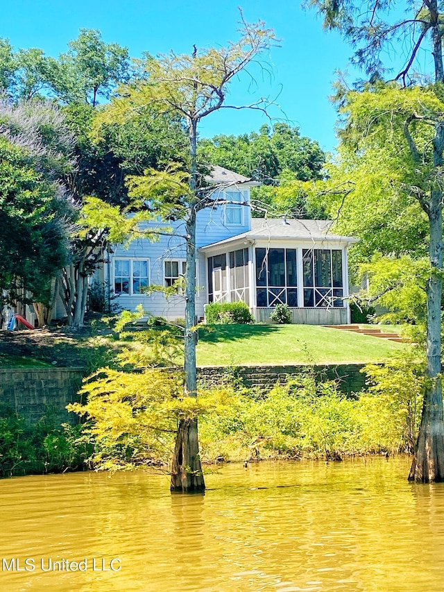 back of property with a sunroom, a lawn, and a water view