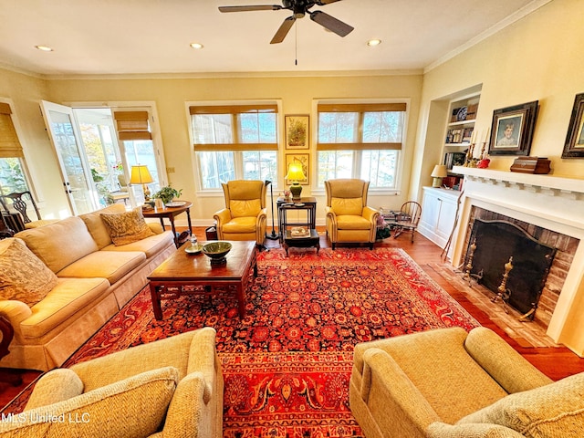 living area with healthy amount of natural light, crown molding, wood finished floors, a ceiling fan, and a high end fireplace