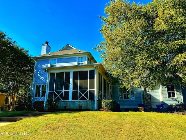 back of property with a sunroom, a chimney, and a yard