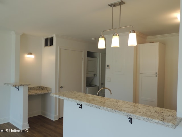 kitchen with a breakfast bar, dark wood-style flooring, stacked washer / dryer, visible vents, and crown molding