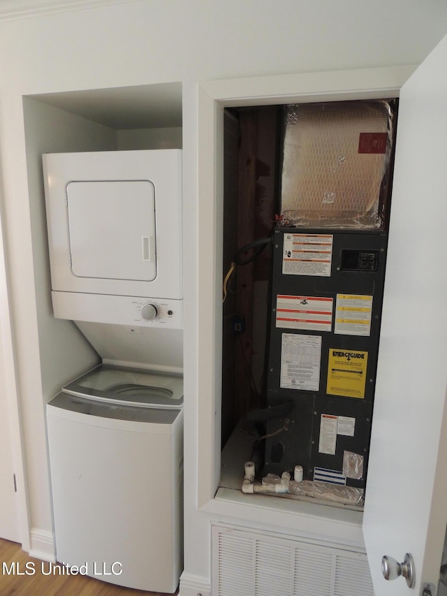 washroom featuring stacked washer and dryer, wood finished floors, laundry area, and heating unit