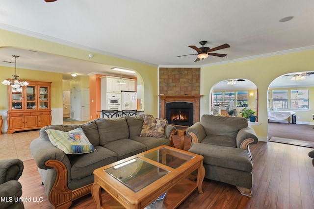 living room with a large fireplace, light wood finished floors, arched walkways, a ceiling fan, and ornamental molding