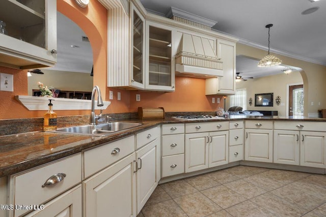 kitchen featuring arched walkways, crown molding, hanging light fixtures, glass insert cabinets, and a sink