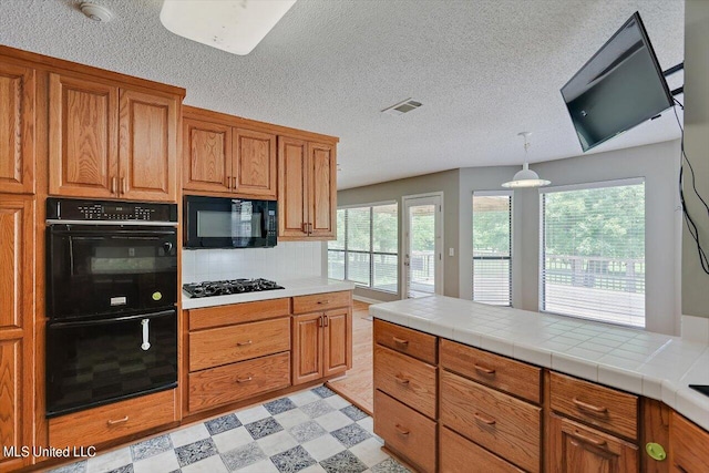 kitchen with black appliances, tile countertops, backsplash, a textured ceiling, and hanging light fixtures