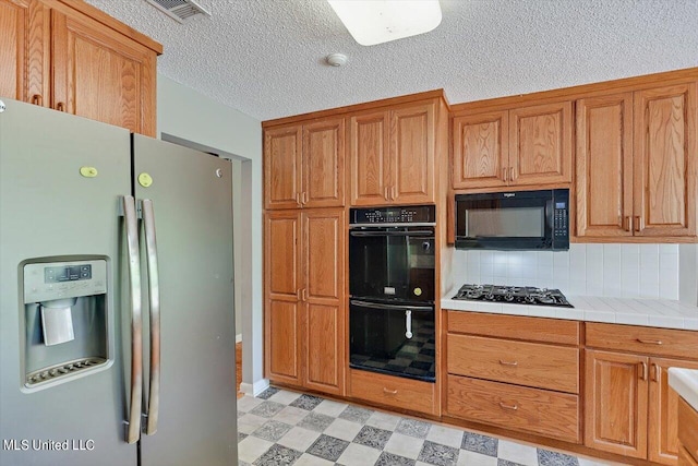 kitchen with decorative backsplash, black appliances, a textured ceiling, and tile counters