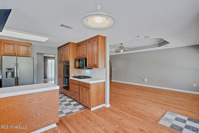 kitchen with tile counters, black appliances, hanging light fixtures, and light wood-type flooring