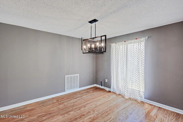 unfurnished dining area with hardwood / wood-style flooring, a textured ceiling, and an inviting chandelier