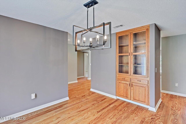 unfurnished dining area with a textured ceiling, light hardwood / wood-style flooring, and a chandelier