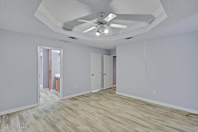 spare room featuring light hardwood / wood-style flooring, a textured ceiling, a raised ceiling, and ceiling fan