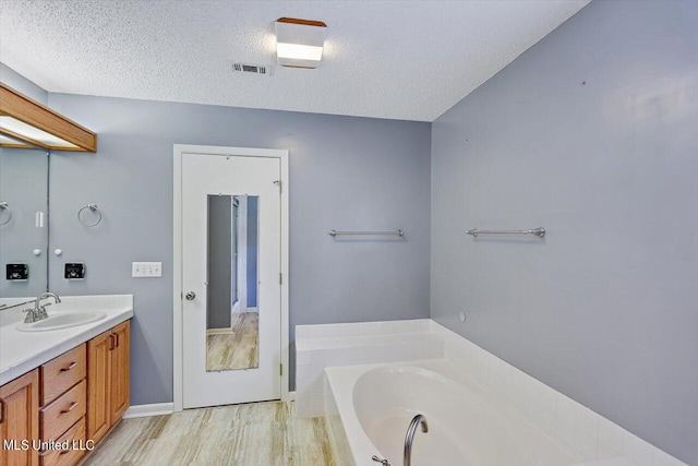 bathroom with vanity, a tub to relax in, a textured ceiling, and hardwood / wood-style floors