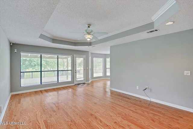 empty room with plenty of natural light, crown molding, light wood-type flooring, and a raised ceiling