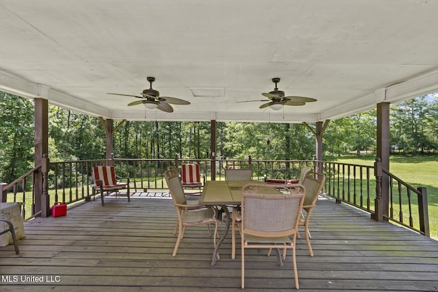 wooden terrace featuring ceiling fan, outdoor dining area, a lawn, and view of scattered trees