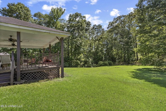 view of green lawn featuring a ceiling fan and a deck