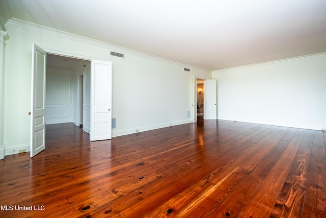 empty room featuring crown molding, dark wood-style flooring, baseboards, and visible vents