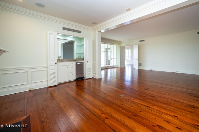 unfurnished living room featuring ornamental molding, dark wood finished floors, wainscoting, visible vents, and a decorative wall