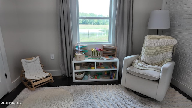 sitting room with brick wall and hardwood / wood-style flooring