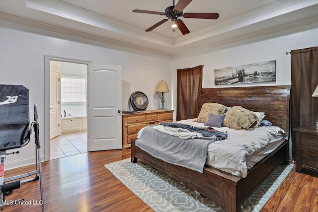 bedroom featuring crown molding, a raised ceiling, wood finished floors, and connected bathroom