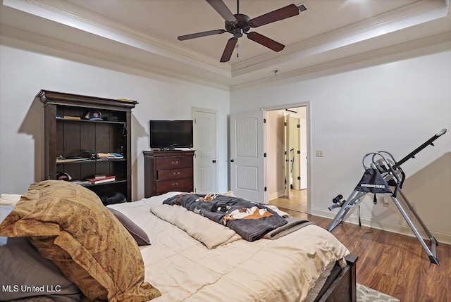 bedroom featuring baseboards, ornamental molding, wood finished floors, and a tray ceiling