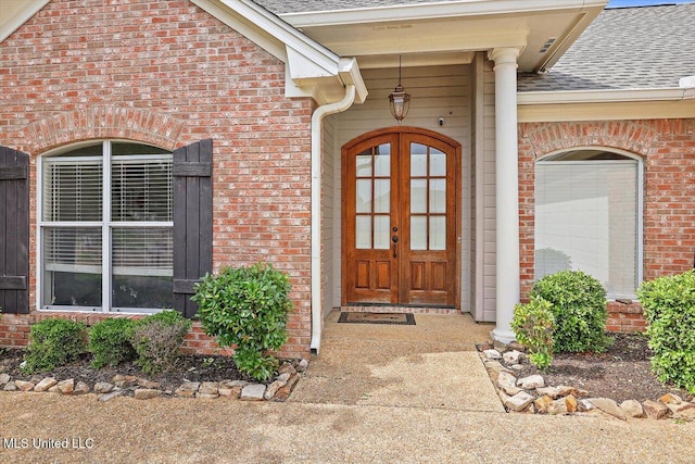 view of exterior entry with brick siding and a shingled roof