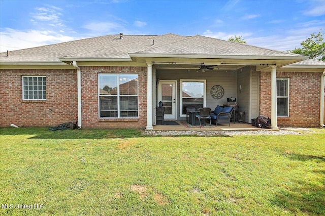 back of property with ceiling fan, a patio, brick siding, a shingled roof, and a lawn