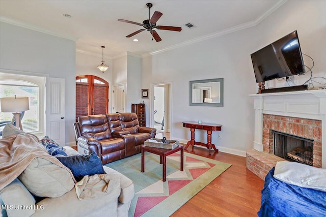 living area with ceiling fan, visible vents, arched walkways, a brick fireplace, and wood finished floors