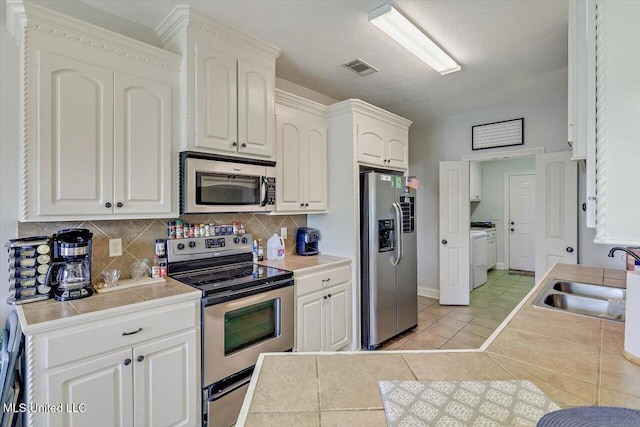 kitchen featuring light tile patterned flooring, appliances with stainless steel finishes, a sink, decorative backsplash, and visible vents