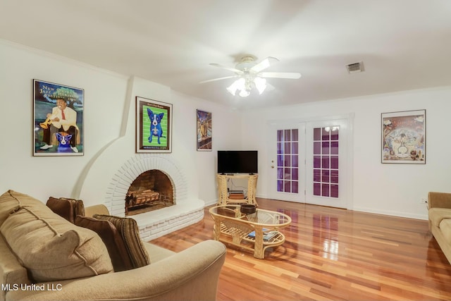 living room featuring wood finished floors, visible vents, baseboards, a ceiling fan, and a brick fireplace