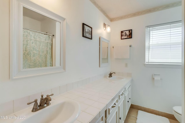 bathroom featuring toilet, double vanity, baseboards, and a sink