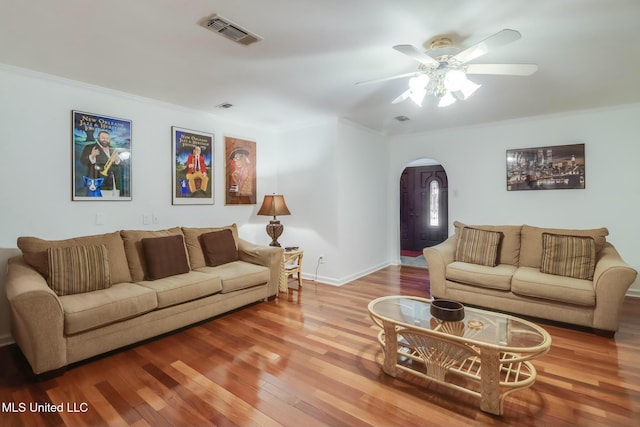 living room featuring arched walkways, crown molding, visible vents, ceiling fan, and wood finished floors