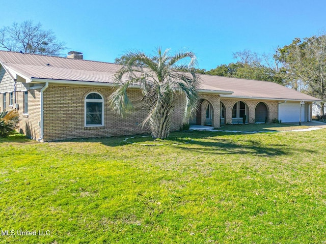 view of front of property featuring metal roof, a garage, brick siding, a front lawn, and a chimney