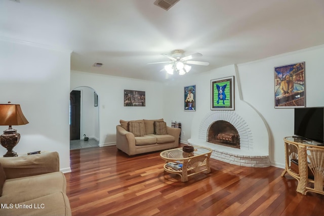 living room featuring arched walkways, a brick fireplace, wood finished floors, and visible vents