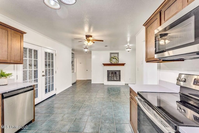 kitchen with light tile patterned flooring, ceiling fan, stainless steel appliances, a brick fireplace, and french doors