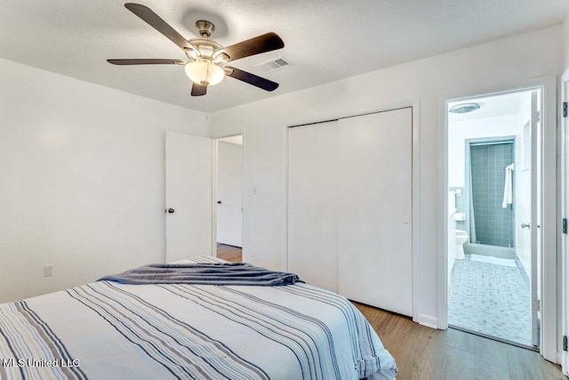 bedroom with ensuite bathroom, ceiling fan, light wood-type flooring, and a closet