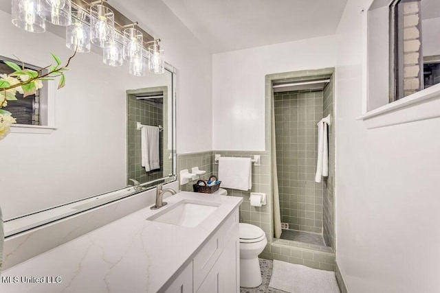 bathroom with vanity, tile walls, toilet, and tiled shower