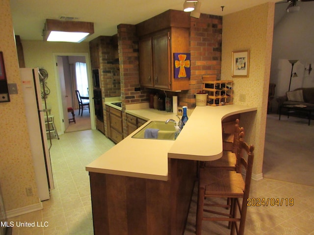 kitchen with sink, a kitchen bar, white fridge, and kitchen peninsula