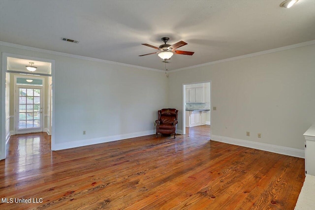empty room featuring ornamental molding, wood finished floors, visible vents, and ceiling fan