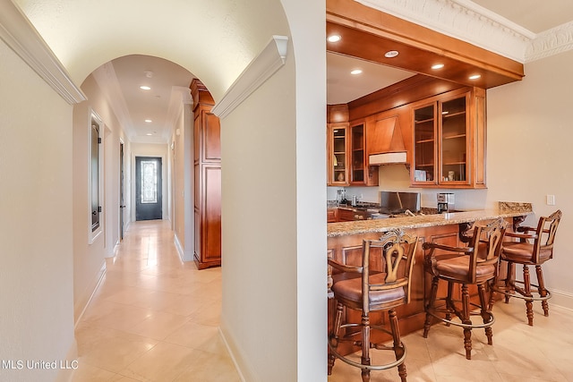 bar featuring crown molding, light stone countertops, custom range hood, and light tile patterned floors