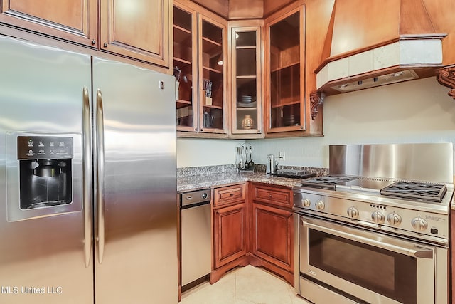 kitchen featuring light stone countertops, premium range hood, appliances with stainless steel finishes, and light tile patterned flooring