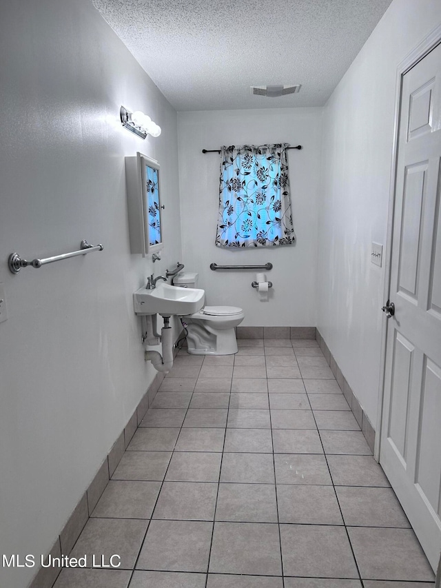 bathroom with toilet, a textured ceiling, sink, and tile patterned floors